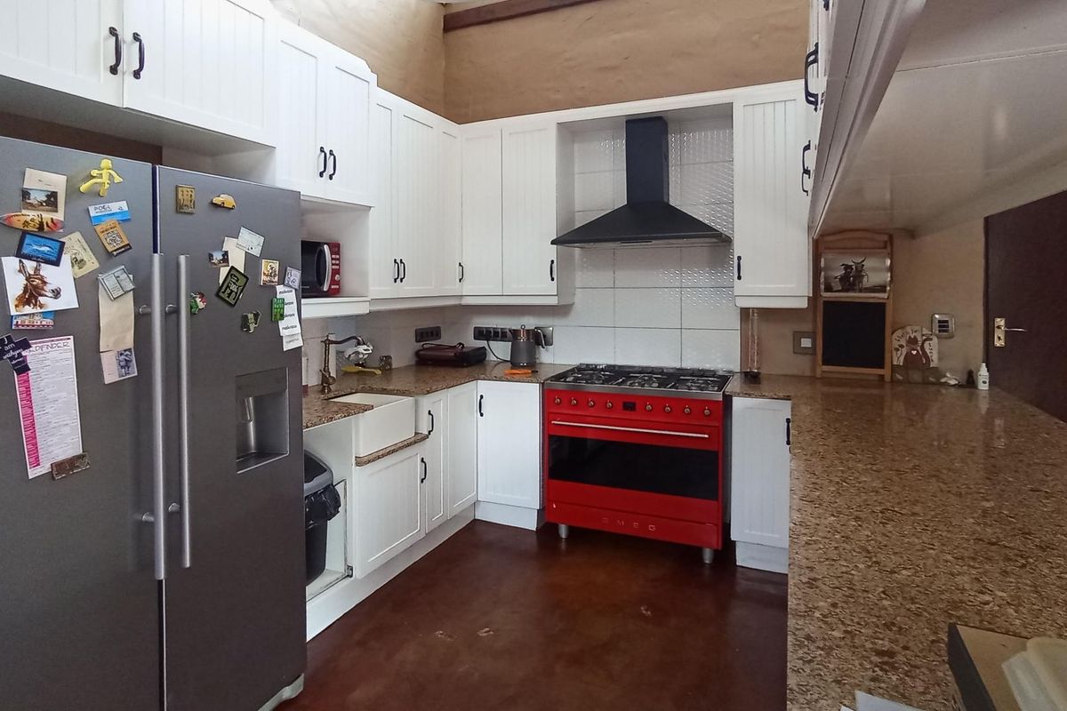 A functional kitchen featuring white cabinetry, granite countertops, a farmhouse sink, and a prominent red gas stove with an extractor fan.