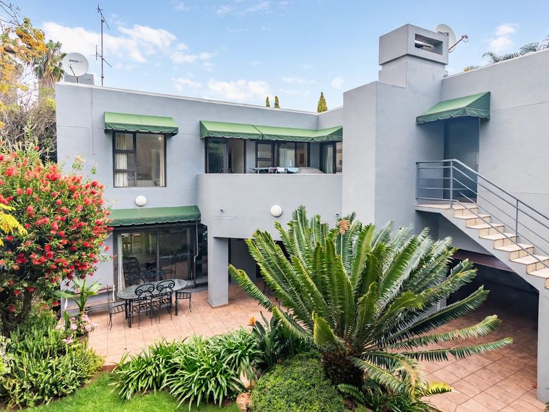 Rear elevation of a two-story house featuring a tiled patio, external staircase, and green canvas awnings overlooking a landscaped garden.