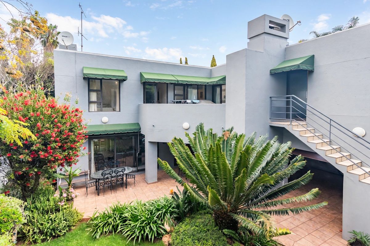 Rear elevation of a two-story house featuring a tiled patio, external staircase, and green canvas awnings overlooking a landscaped garden.