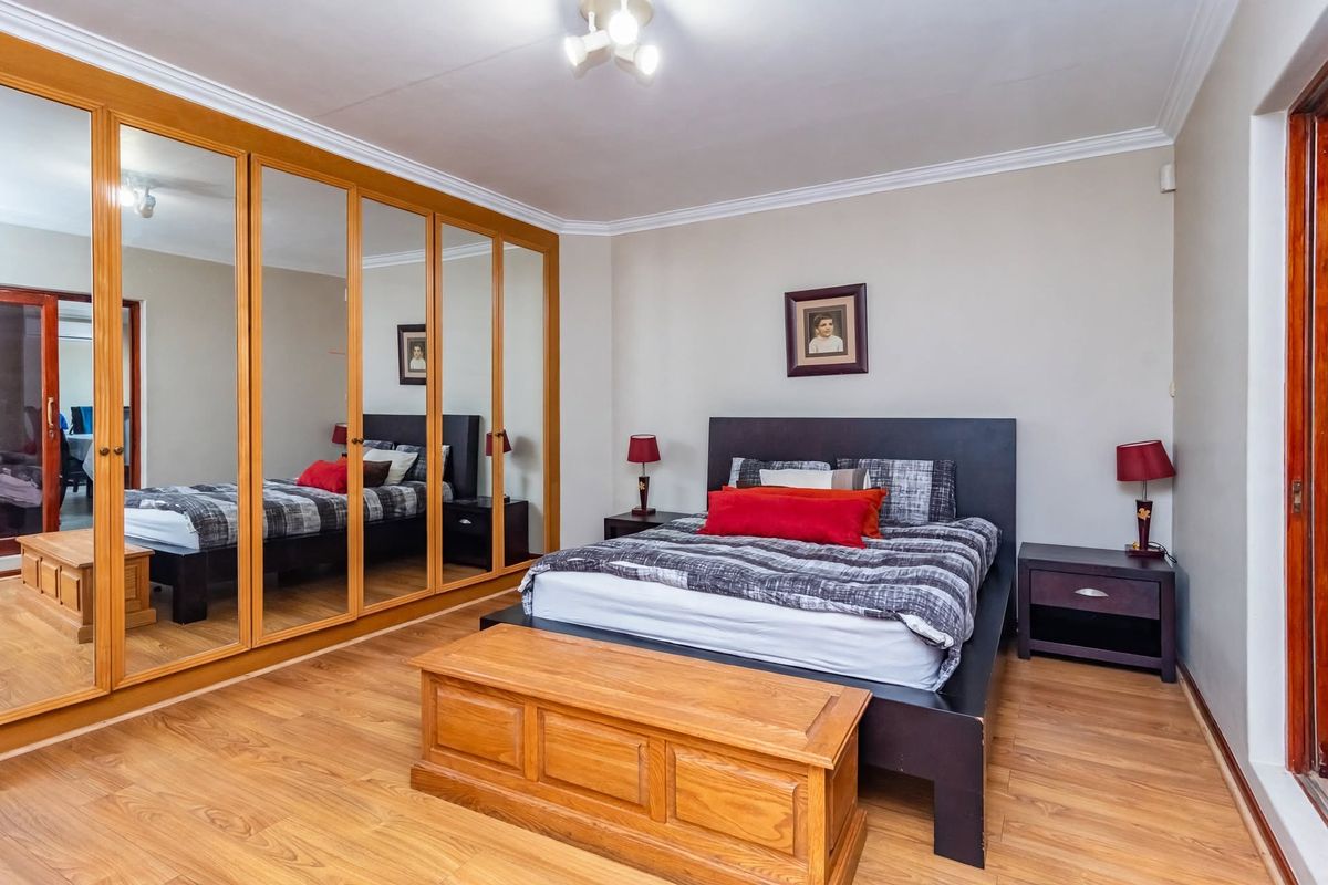 A well-proportioned bedroom featuring laminate flooring, coved ceilings, and a large built-in wardrobe with mirrored doors providing ample storage space.