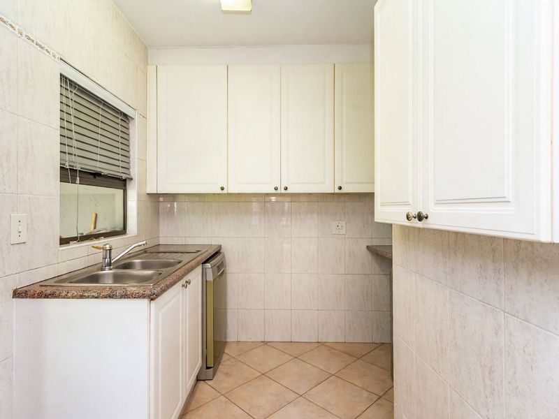 A functional scullery featuring built-in cabinetry, a double sink with granite countertops, and tiled finishes throughout.