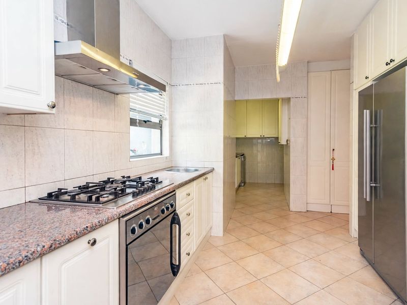 A functional kitchen featuring granite countertops, a gas hob, built-in oven, stainless steel extractor fan, and ample cabinetry with an adjacent scullery area.