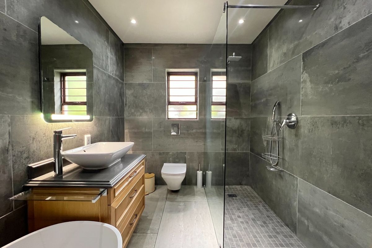 Modern bathroom featuring a spacious walk-in shower with glass screen, wall-mounted toilet, and a stylish vessel sink set on a wooden vanity cabinet.