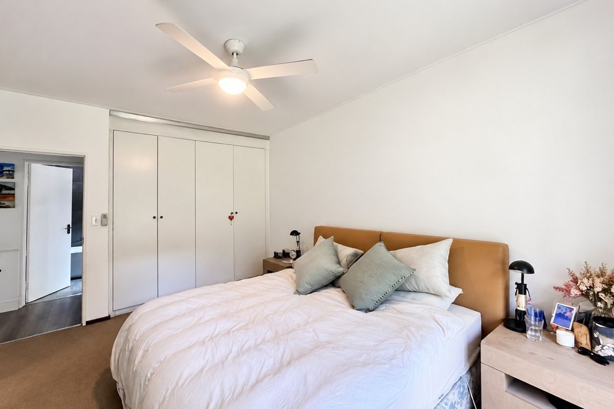 A well-maintained bedroom featuring neutral carpet flooring, a ceiling fan, and ample storage with built-in wardrobes.