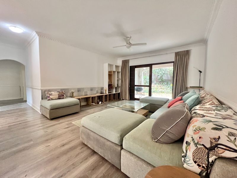 Spacious living room featuring laminate flooring, crown molding, a ceiling fan, and large sliding glass doors providing access to the outdoor area.