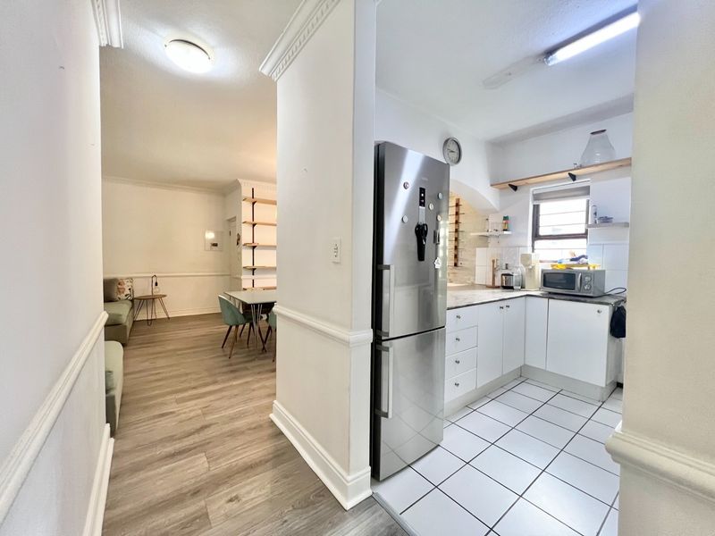 Open plan living area featuring a compact kitchen with white cabinetry, laminate flooring, and classic crown molding details throughout the space.