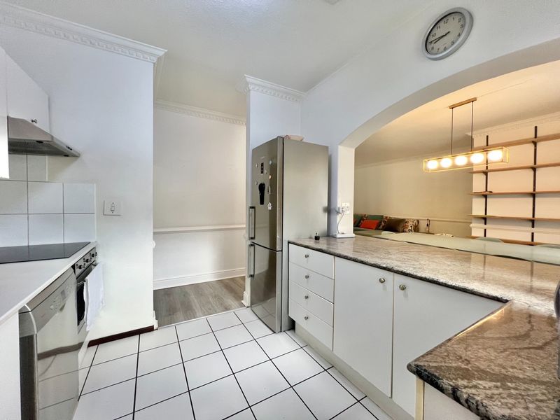 A well-maintained kitchen featuring granite countertops, built-in oven, electric hob, and extractor fan, with an open-plan flow into the adjacent living area.