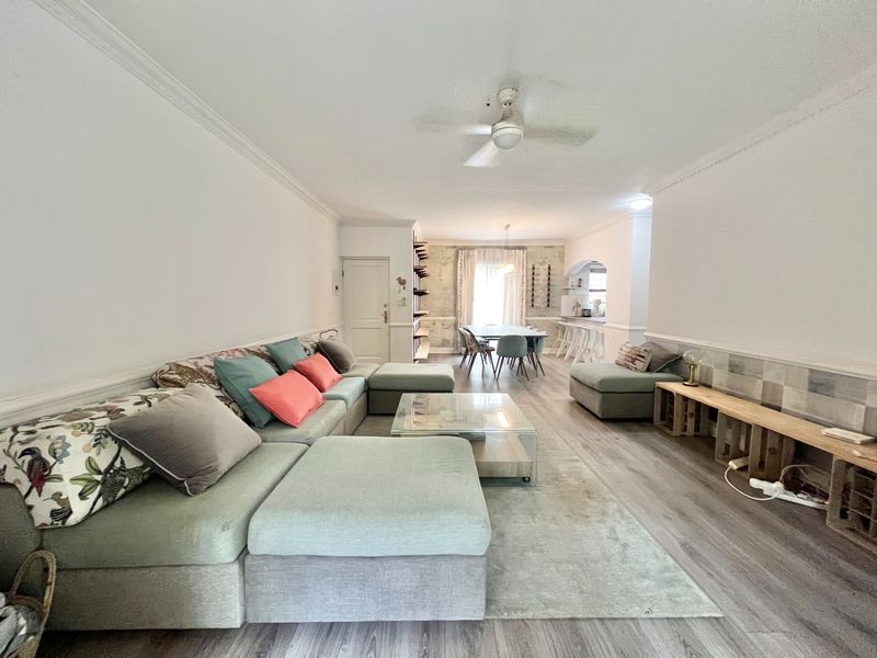 Spacious open-plan living and dining area featuring laminate flooring, crown molding, wainscoting, and a ceiling fan, leading to a kitchen space.