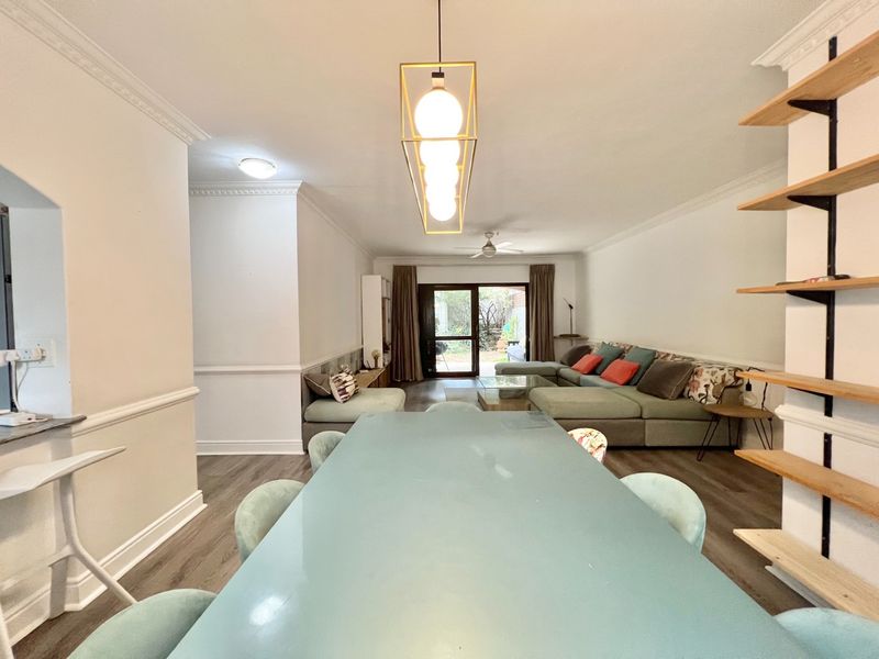 Spacious open-plan living and dining area featuring laminate flooring, crown molding, wainscoting, and a sliding glass door leading to the outdoor space.