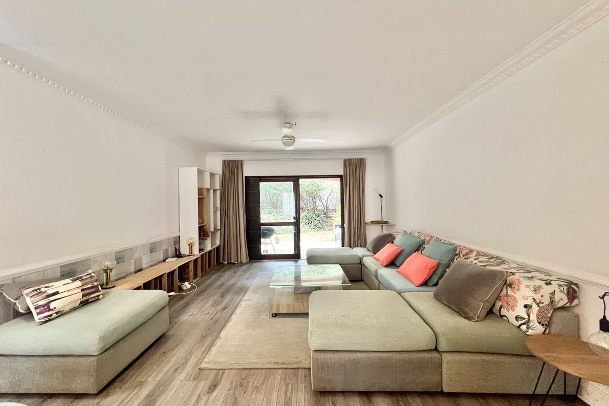 Spacious living room featuring laminate flooring, crown molding, a ceiling fan, and a sliding glass door providing access to the outdoor area.