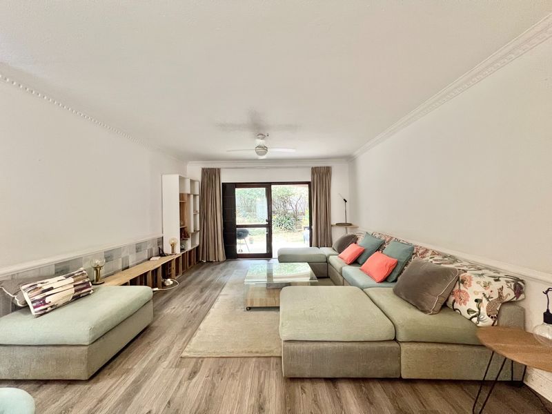 Spacious living room featuring laminate flooring, crown molding, a ceiling fan, and a sliding glass door providing access to the outdoor area.