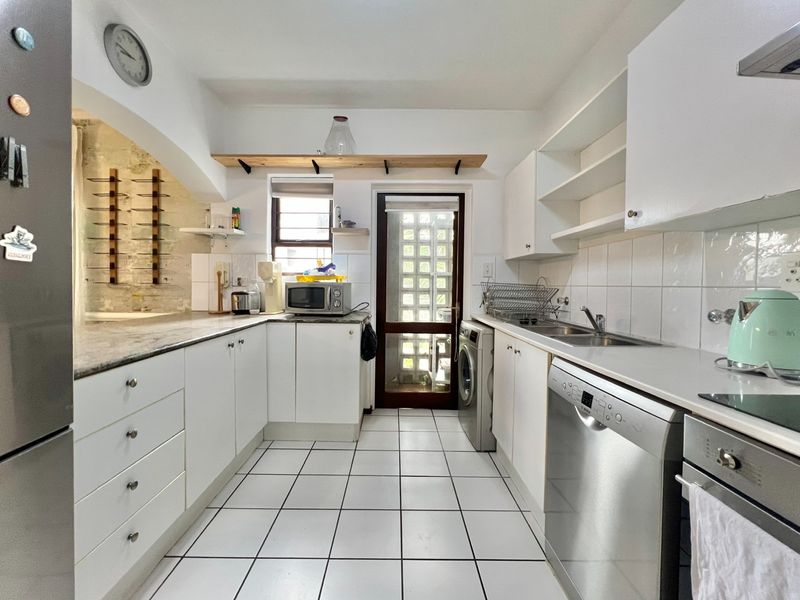 Functional kitchen featuring white cabinetry, stone countertops, tiled backsplash, and integrated appliances, with an archway leading to an adjacent space.