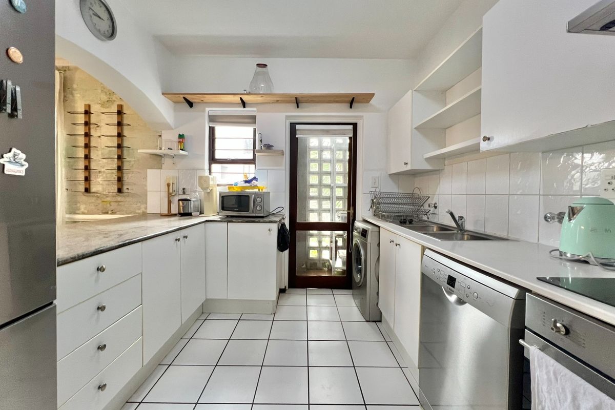 Functional kitchen featuring white cabinetry, stone countertops, tiled backsplash, and integrated appliances, with an archway leading to an adjacent space.
