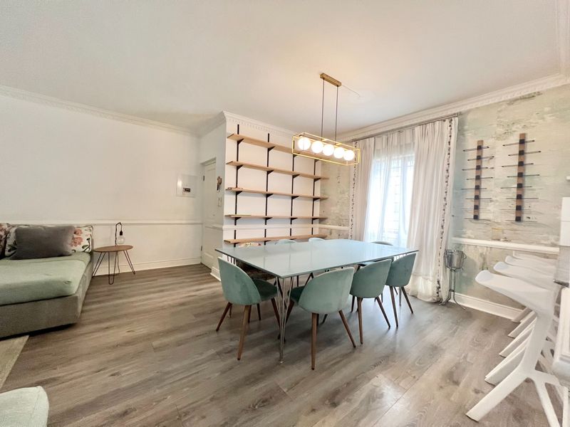 Open plan living and dining area featuring laminate flooring, decorative wall molding, crown molding, and built-in shelving with a modern pendant light fixture.