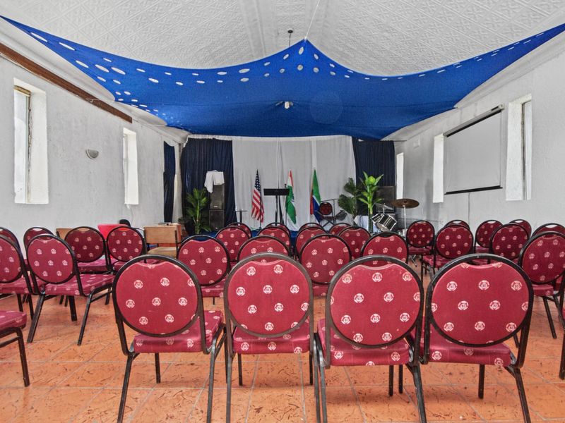 A multi-purpose commercial hall featuring a decorative pressed metal ceiling, tiled flooring, and a built-in projection screen, suitable for meetings or events.