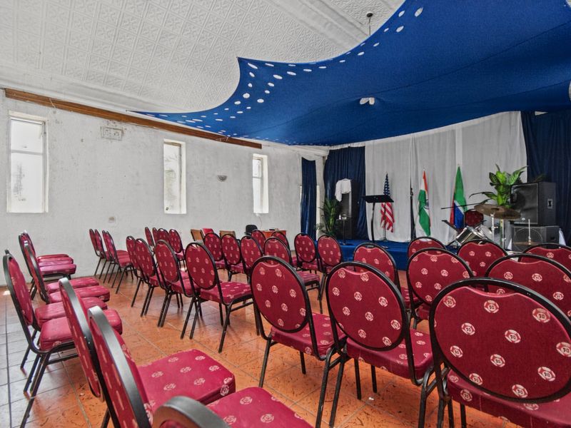 A multi-purpose commercial hall featuring a raised stage, decorative pressed metal ceiling, and tiled flooring, suitable for events or community gatherings.