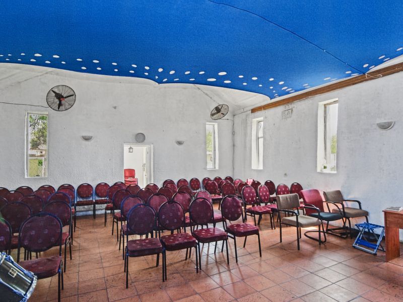 A multi-purpose hall or clubhouse space featuring tiled flooring, wall-mounted fans, and a decorative blue ceiling canopy, suitable for community or commercial gatherings.