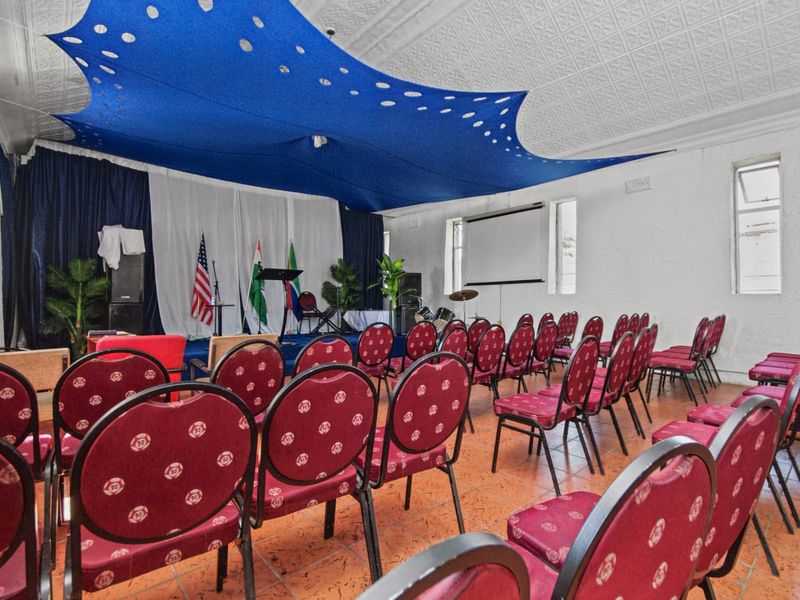 A multi-purpose commercial hall featuring a raised stage area, projector screen, and decorative pressed metal ceiling, suitable for events or community gatherings.