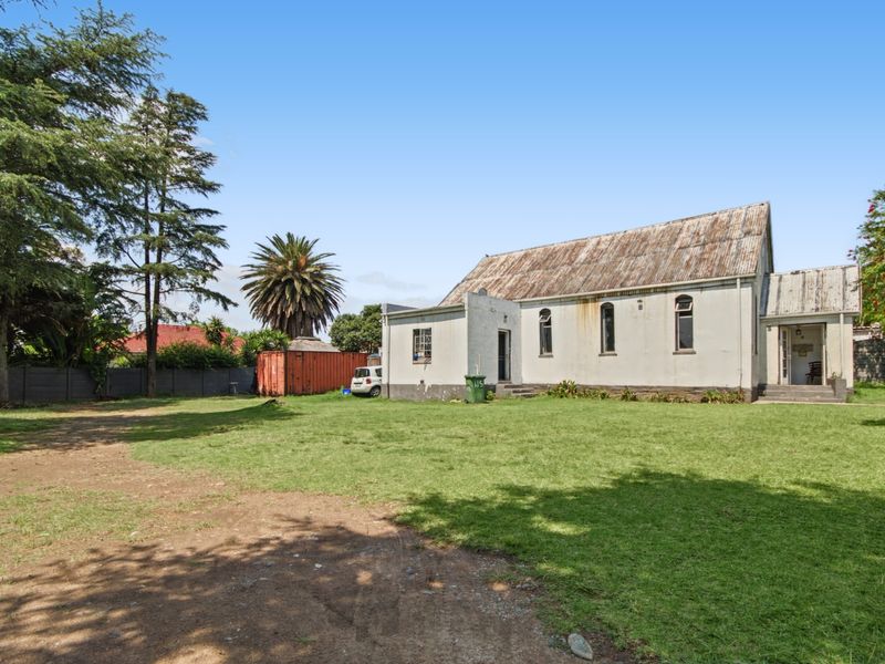Rear view of a commercial building featuring a corrugated metal roof, arched windows, and a large surrounding lawn area.