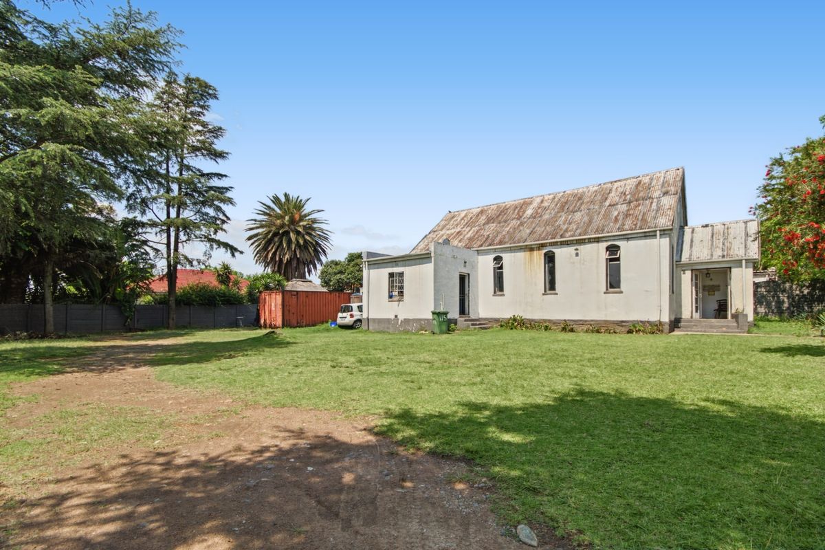 Rear view of a commercial building featuring a corrugated metal roof, arched windows, and a large surrounding lawn area.