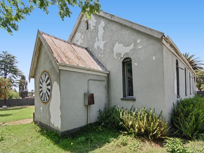 Rear exterior view of a commercial building featuring a corrugated metal roof, arched windows, and significant exterior paint deterioration requiring maintenance.