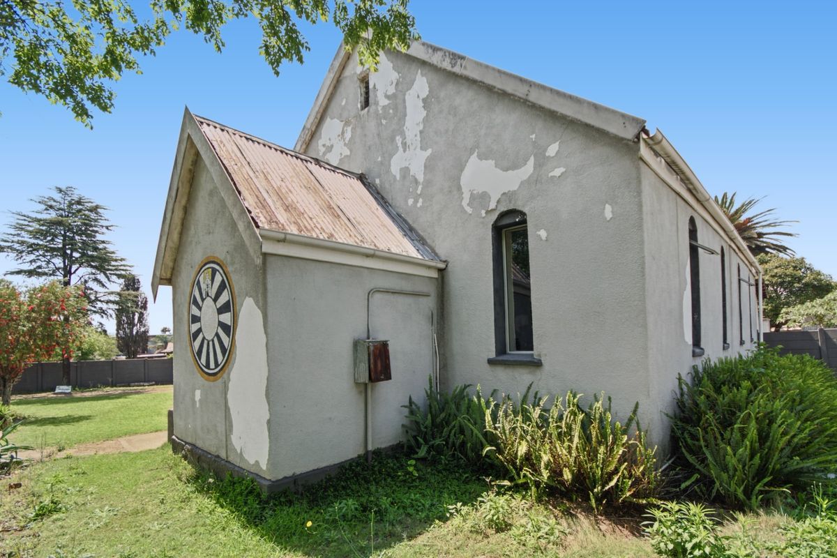 Rear exterior view of a commercial building featuring a corrugated metal roof, arched windows, and significant exterior paint deterioration requiring maintenance.