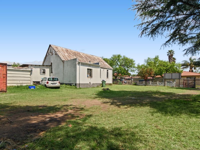 Rear view of the commercial property featuring a large open yard area, metal roofing, and perimeter security fencing.