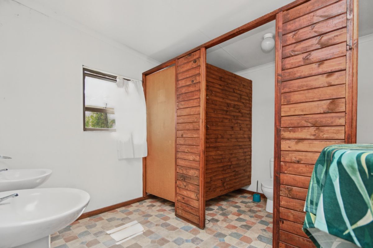 A functional bathroom featuring dual pedestal sinks, a toilet, and a wooden partition wall, finished with patterned vinyl flooring.