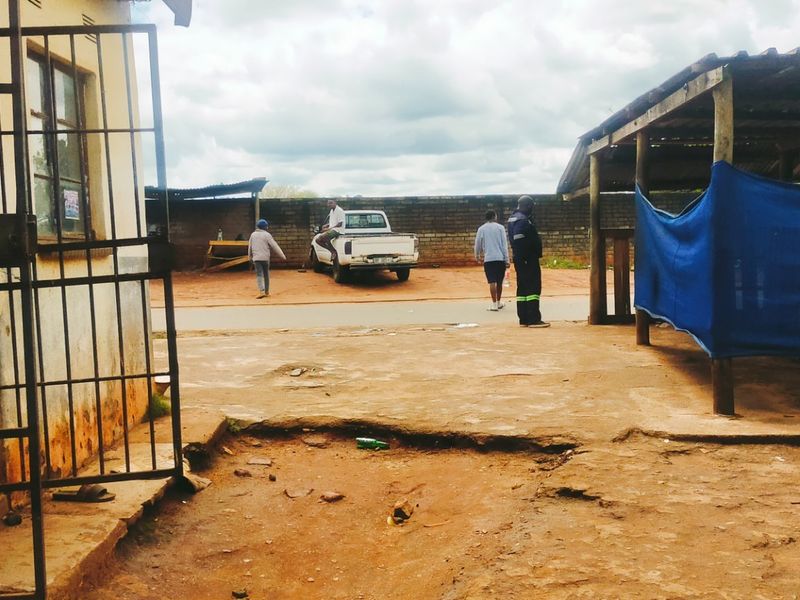 An outdoor business yard area featuring a security gate, a timber-framed structure, and a brick boundary wall with an uneven, unpaved ground surface.
