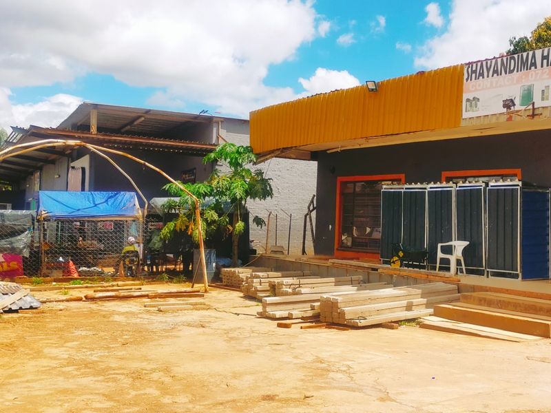 Front exterior view of a commercial hardware store featuring a concrete loading area, corrugated metal roofing, and prominent business signage.