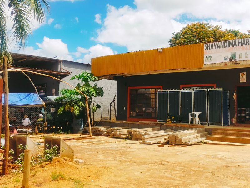Front exterior view of a commercial hardware store featuring a metal roof, concrete entrance steps, and prominent business signage.