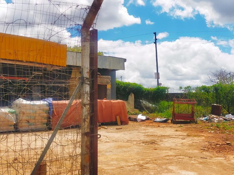 Exterior view of a commercial property featuring a concrete yard, chain-link perimeter fencing, and a building structure with existing signage.