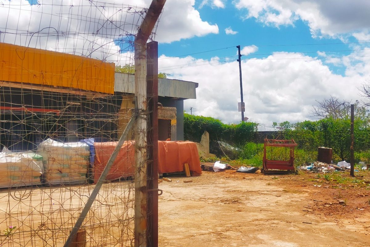 Exterior view of a commercial property featuring a concrete yard, chain-link perimeter fencing, and a building structure with existing signage.