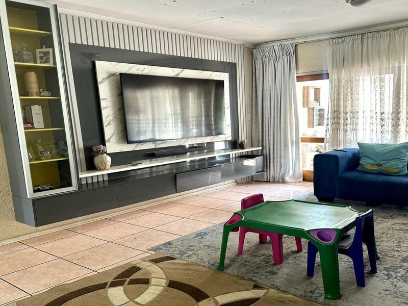 Spacious living room featuring a modern built-in media wall unit, tiled flooring, and direct access to an outdoor area through sliding glass doors.