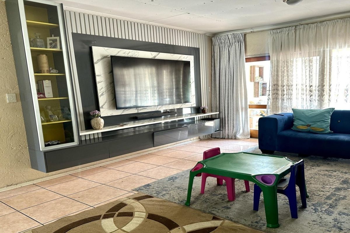 Spacious living room featuring a modern built-in media wall unit, tiled flooring, and direct access to an outdoor area through sliding glass doors.