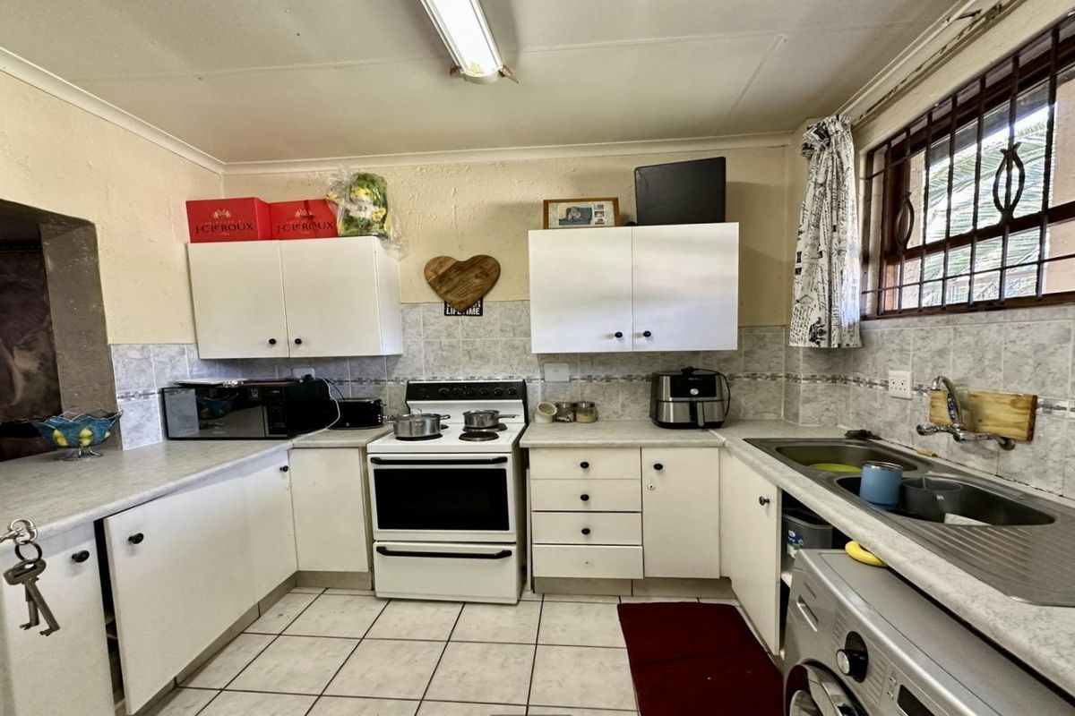 A functional kitchen featuring white cabinetry, tiled backsplash, laminate countertops, and a freestanding stove, with security bars installed on the window.