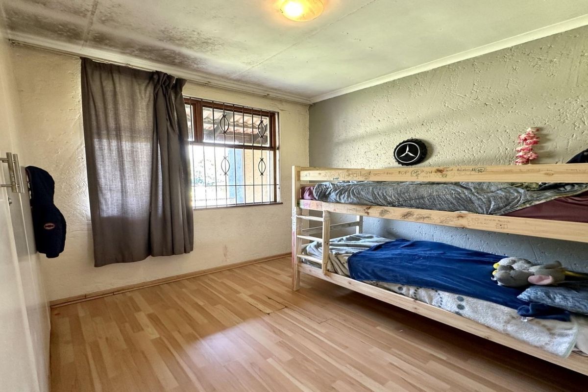 A bedroom featuring laminate flooring and security bars on the window, currently showing significant signs of ceiling water damage and wall surface deterioration.
