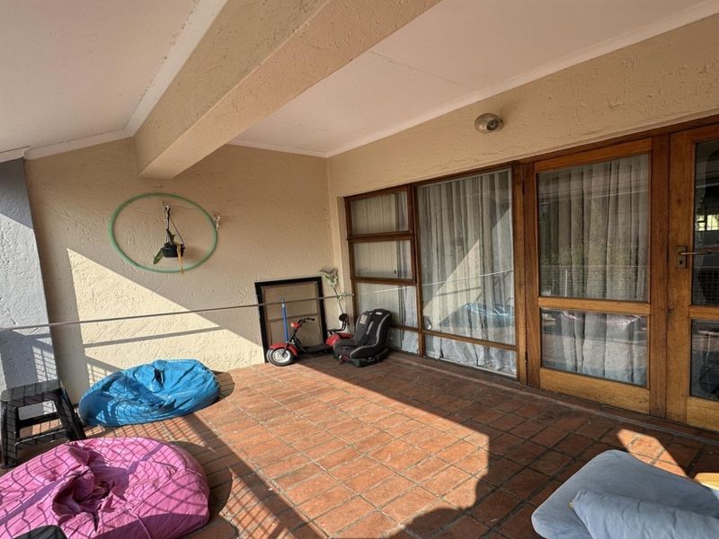 A spacious covered balcony featuring terracotta tile flooring and timber-framed sliding doors, offering a functional outdoor living area.
