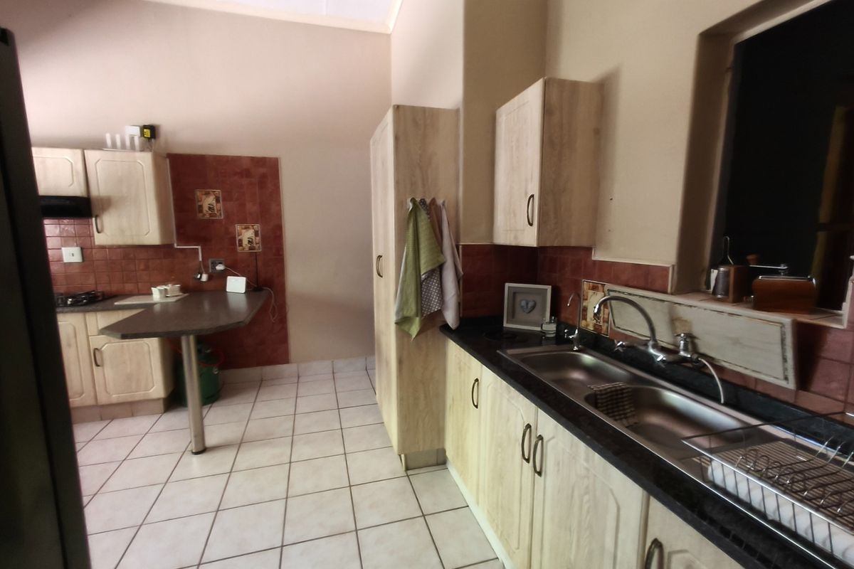 A functional kitchen featuring light wood-finish cabinetry, dark laminate countertops, a double basin sink, and tiled backsplash with neutral floor tiles.
