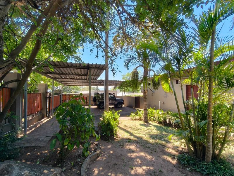 A well-maintained front exterior featuring a paved driveway, a functional metal carport, and established garden landscaping.
