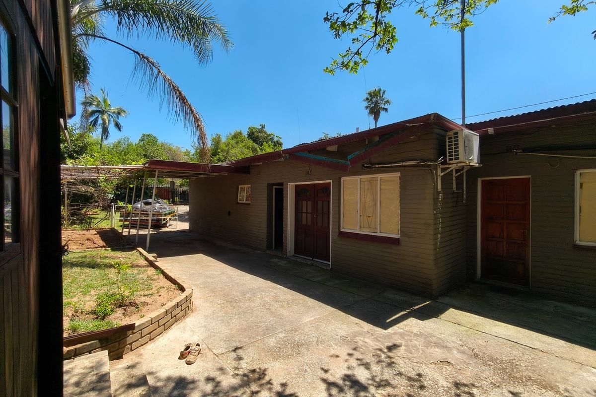 Rear exterior view of the property featuring a concrete driveway, covered carport area, and brick facade with established garden surroundings.
