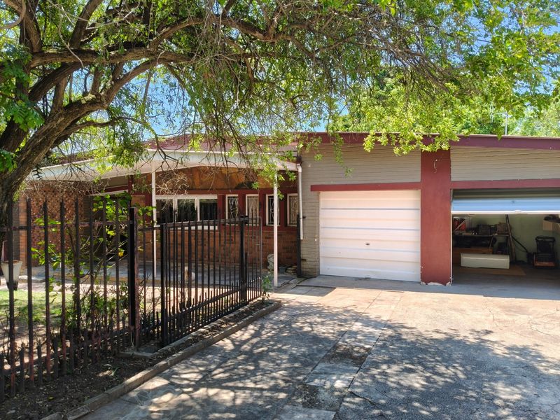 Front elevation of a single-story house featuring a brick facade, covered porch, attached garage, and a concrete driveway with security fencing.