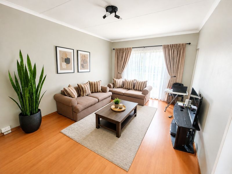 A well-maintained living room featuring laminate flooring, neutral wall tones, and large windows with curtain treatments, providing a bright and comfortable living space.