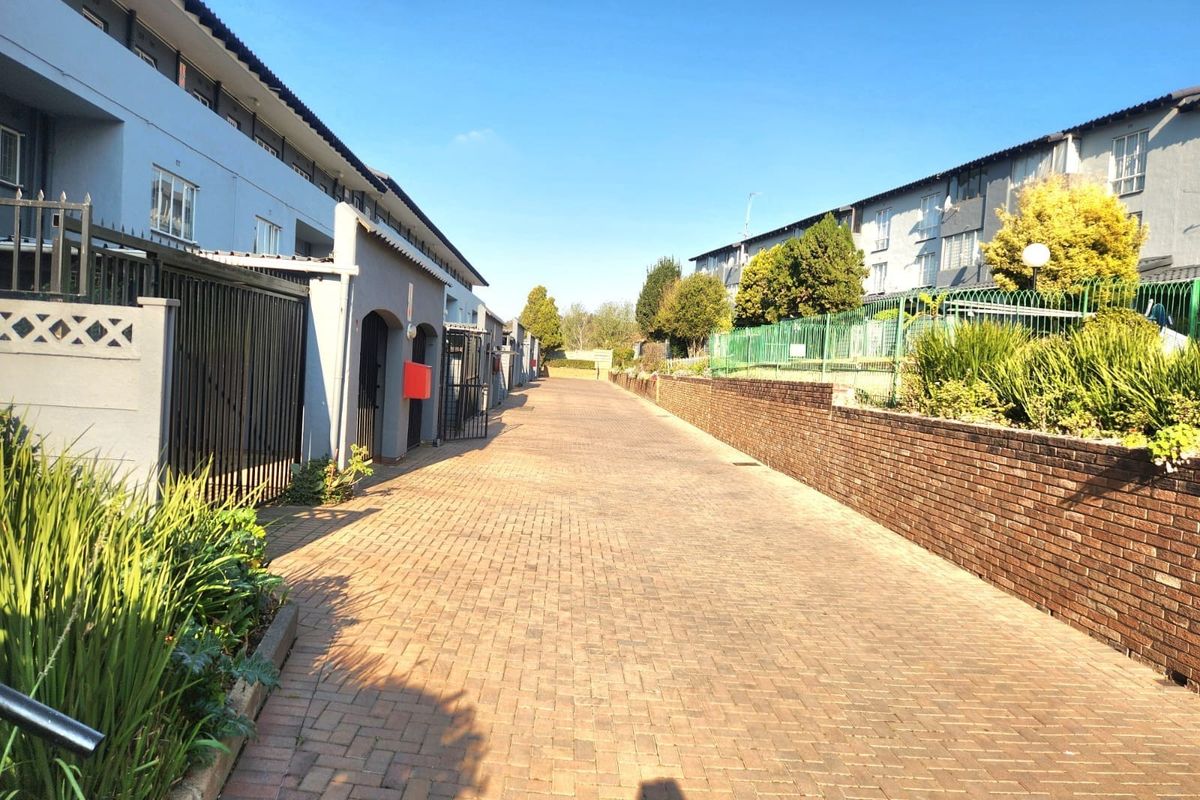 A view of the paved driveway and rear access area of the apartment complex, featuring brick retaining walls and secure metal fencing.
