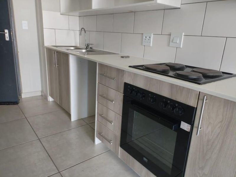 Modern kitchen featuring light wood-grain cabinetry, stone-look countertops, built-in oven and hob, and clean white subway tile backsplash.