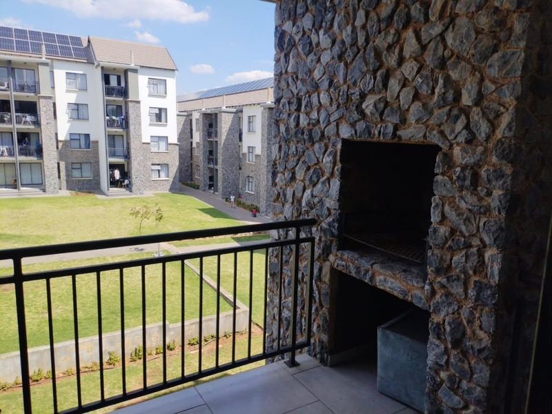 A spacious balcony featuring a built-in stone-clad braai, metal balustrade, and tiled flooring, overlooking the apartment complex grounds.