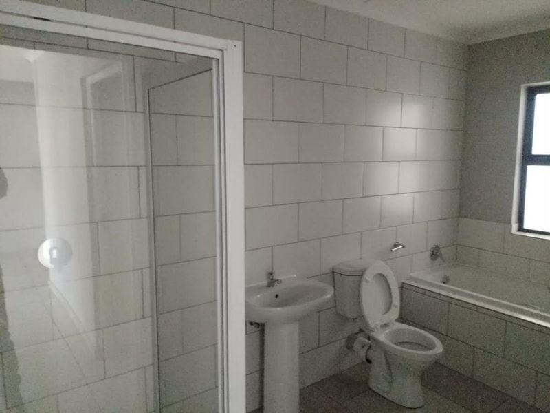 A clean, modern bathroom featuring a pedestal basin, toilet, built-in bathtub, and a separate shower enclosure with tiled walls.