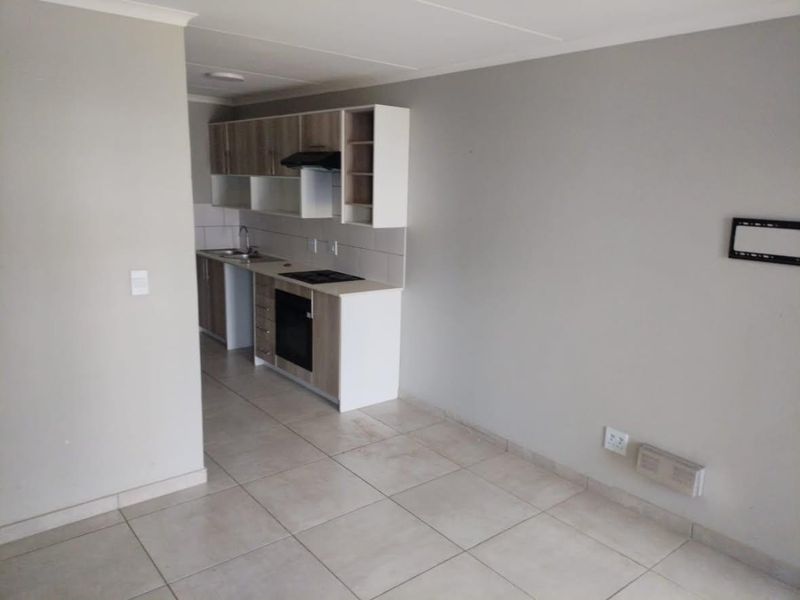An open-plan living and kitchen area featuring neutral tiled flooring, modern built-in cabinetry, and integrated kitchen appliances in a clean, vacant space.