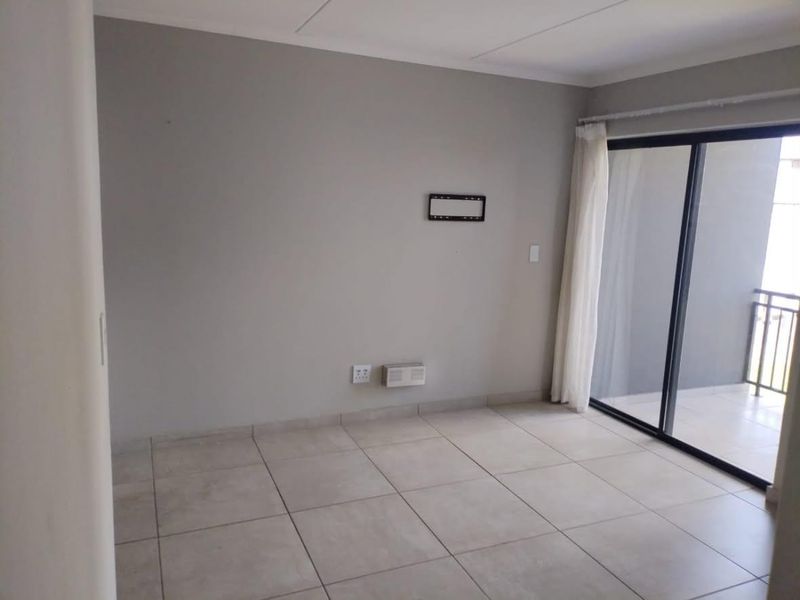 An empty, well-maintained living room featuring neutral tiled flooring and a sliding glass door providing access to an outdoor balcony.