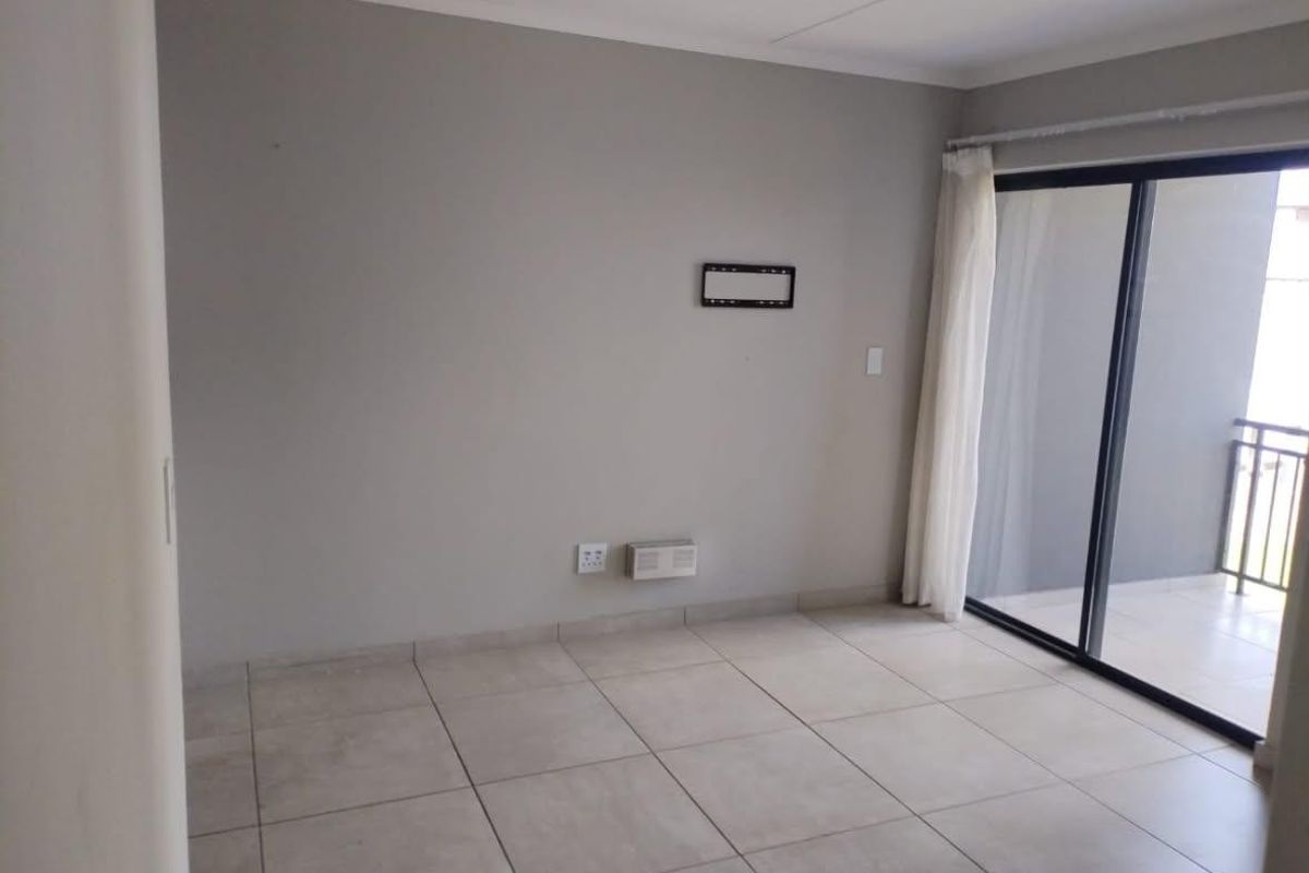 An empty, well-maintained living room featuring neutral tiled flooring and a sliding glass door providing access to an outdoor balcony.